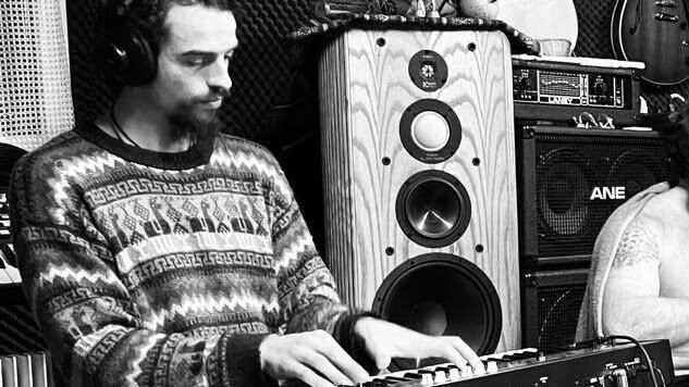 playing a synthesizer in a studio, headphones on, speaker cabinets behind